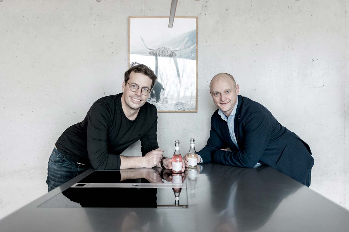 sympatische-gruender-vintonic-vor-wand-mit-vintonic-in-der-hand